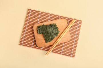 Wooden board with tasty seaweed sheets and chopsticks on yellow background © Pixel-Shot