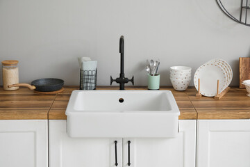 Counters with ceramic sink, kitchen utensils and food near light wall