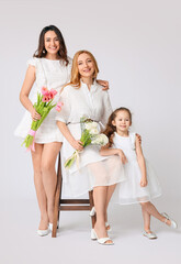 Young woman, her little daughter and mother with flowers on light background. International Women's Day celebration
