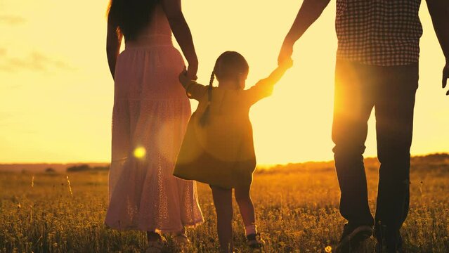 happy cheerful child jumping across field with mother father sunset. happy family together. journey kid child park sun. playground run. mom dad walk with child. parents hold kid by hands against sky