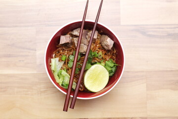 Stewed pork Noodle garnished with coriander, sliced spring onions and lemon wedges. Served on an ash wood table