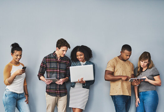 Tapped Into Everything Thats Now. Studio Shot Of A Group Of Young People Using Wireless Technology Against A Gray Background.