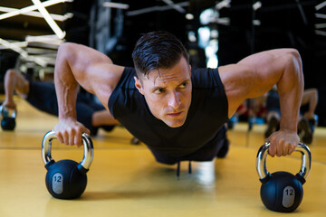 Muscular man in gym doing pushups exercise with kettle-bell in a workout.