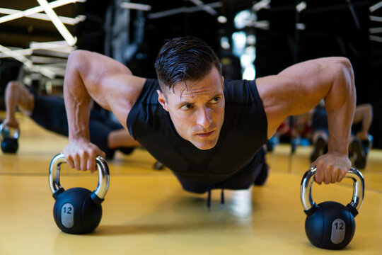 Muscular man in gym doing pushups exercise with kettle-bell in a workout.