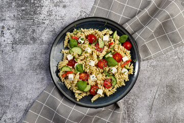 Pasta Salad with tomatoes, bell peppers and feta cheese on a round plate on a dark gray background....