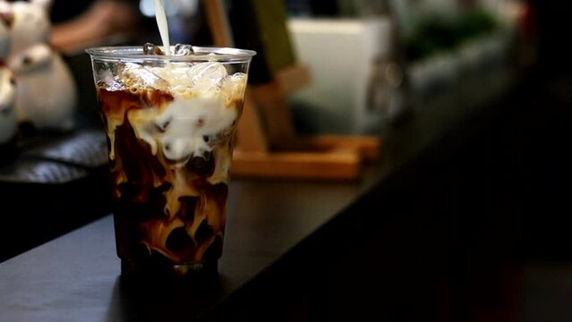 Barista pouring milk into a glass of iced coffee