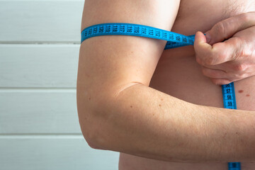 A man measures his biceps and a tape measure.