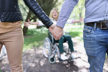 Man and woman hold on to hand and walks away from woman in wheelchair