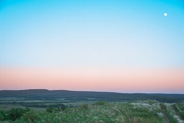 Road, hills, moon and field at sunset.