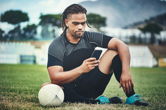 Theres time for rugby then theres time for connectivity. Full length shot of a handsome young rugby player using a smartphone while sitting in the playing field during the day.