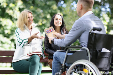 Two women and a man in a wheelchair are learning English while sitting in park