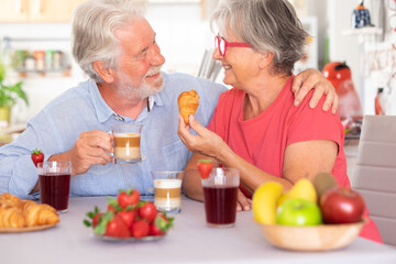 Beautiful senior couple smiling looking each other in the eyes while having breakfast at home with...