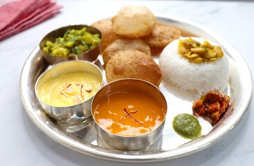 Indian vegetarian lunch or dinner Thali includes Aloo ki sabji, dal rice, Puri bhaji, Shrikhand or Srikhand, Aamras, papad, pickle, and chutney. Indian food is served in a Silverplate or thali. copy.