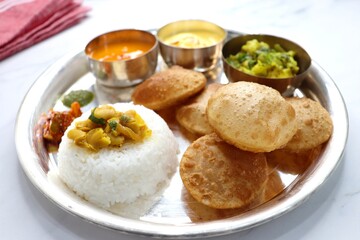 Indian vegetarian lunch or dinner Thali includes Aloo ki sabji, dal rice, Puri bhaji, Shrikhand or Srikhand, Aamras, papad, pickle, and chutney. Indian food is served in a Silverplate or thali. copy.