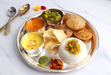 Indian vegetarian lunch or dinner Thali includes Aloo ki sabji, dal rice, Puri bhaji, Shrikhand or Srikhand, Aamras, papad, pickle, and chutney. Indian food is served in a Silverplate or thali. copy.
