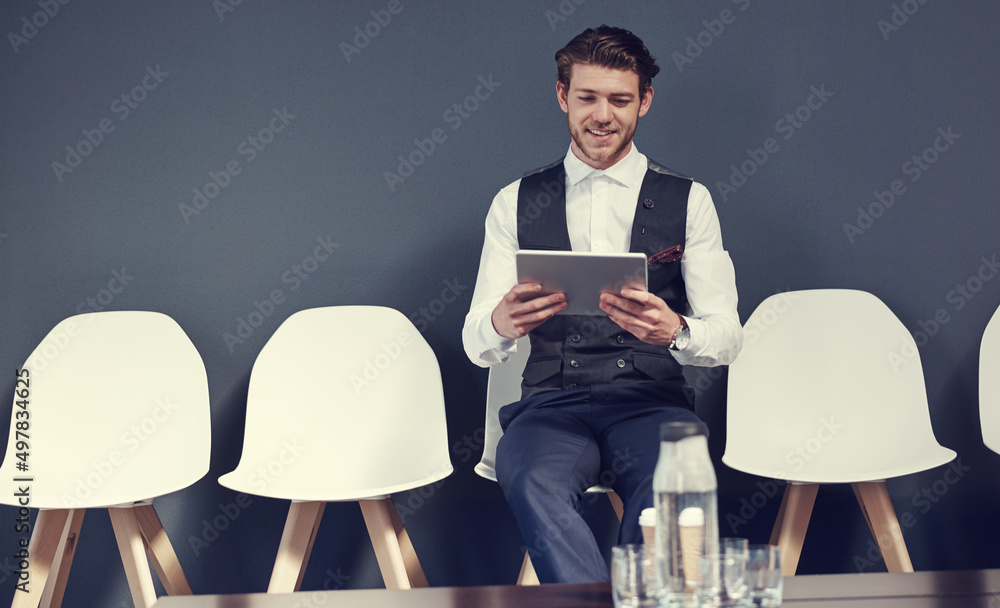 Poster Last minute checks before the interview. Shot of a young businessman using a tablet while waiting for an interview.