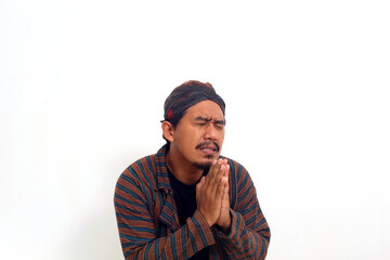 Sad asian man in java traditional costume begging for forgiveness. Isolated on white background