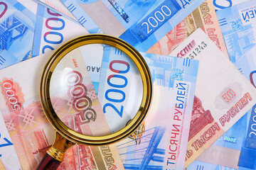 Magnifying magnifier against background Russian rubles denominations five and two thousand.