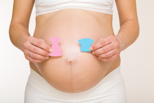 Shapes of pink dress and blue shirt on young adult pregnant woman big naked belly. Guessing future baby gender. Baby expectation. Closeup. Isolated on light gray background. Front view.