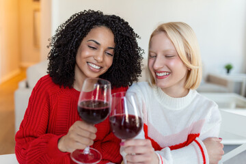Women sitting on sofa laughing in a cozy loft apartment with wine. Two Female Friends Relaxing On Sofa At Home With Glass Of Wine Talking Together.
