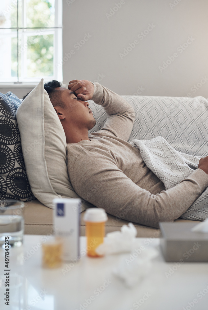 Wall mural Ill just lay here for the day. Shot of a young man experiencing a headache while feeling sick at home.