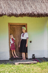 mother and daughter in Ukrainian national costumes stand near the door from the house