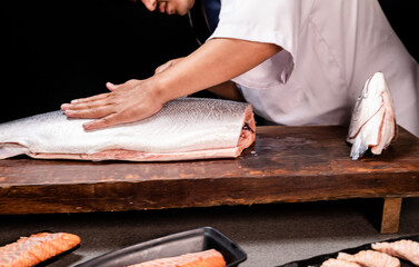Obraz premium Chef's hand holding fresh piece of salmon.Closeup of chef hands preparing japanese food. Japanese chef making sushi at restaurant.Chef making traditional japanese sushi on wood board.