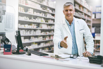 What can I do for you today. Portrait of a cheerful mature male pharmacist reaching out to give a handshake while looking at the camera.