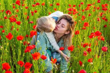 Mother with daughter outdoor in poppy field. Mom hugs lovely child on poppies background. Family in the field of spring blossom flowering meadow. Woman and child laugh and hug. Spring design.