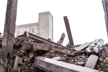 A pile of concrete rubble and construction debris with huge concrete beams against the background of the remains of the building and the gray sky in a hazy haze. Background