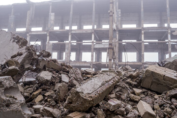 A pile of large concrete fragments against the background of the destroyed frame of the building in...