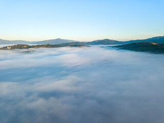 Obraz na płótnie Canvas Flight over fog in Ukrainian Carpathians in summer. Mountains on the horizon. A thick layer of fog covers the mountains with a continuous carpet. Aerial drone view.