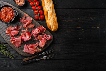 Slices of prosciutto di parma or jamon serrano set, on black wooden background, top view flat lay, with copy space for text - obrazy, fototapety, plakaty