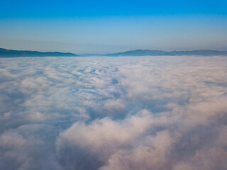 Flight over fog in Ukrainian Carpathians in summer. Mountains on the horizon. Aerial drone view.