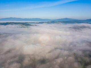 Flight over fog in Ukrainian Carpathians in summer. Mountains on the horizon. Aerial drone view.