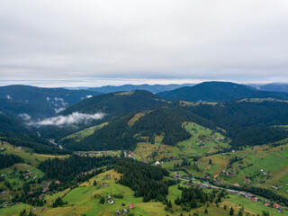 Green slopes of Ukrainian Carpathian mountains in summer. Cloudy morning, low clouds. Aerial drone view.