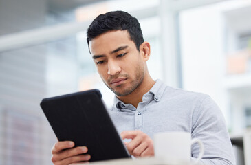 Always stay informed. Shot of a young businessman drinking coffee while using his digital tablet.