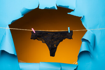 Black panties on rope. Lace underwear. Womans black erotic panties. Womens panties hanging isolated on paper hole background.