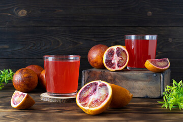 Juice from a Sicilian orange in low transparent glasses on a wooden table. Half an orange and a glass on a wooden box. Green twigs on the table. Wooden background