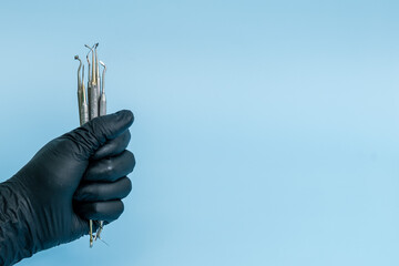 Cropped shot of professional dentist in black medical gloves with dental tools. Dental concept. Isolated on blue background