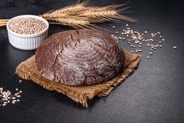 Fresh baked homemade brown bread on a black concrete background with wheat grains