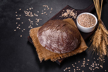 Fresh baked homemade brown bread on a black concrete background with wheat grains