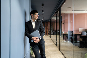 A financier with glasses, a man in formal clothes, works in an office in a coworking, holding a laptop in his hands
