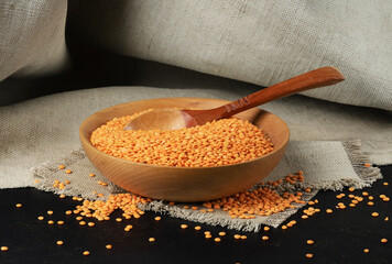 A bowl of red lentils on a rough napkin with a dark background.