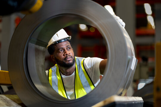 African American engineer worker is examining the stainless galvanized metal sheet roll inside the warehouse factory for roofing industry concept