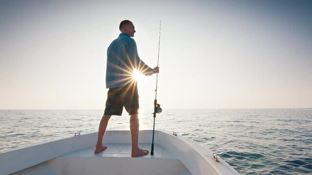 Open sea fishing. Angler stands with fishing rod on the boat floating in the open sea and looks somewhere