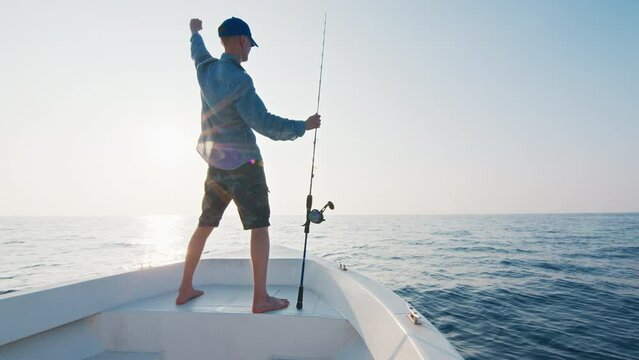 Open sea fishing. Angler stands with fishing rod on the boat floating in the open sea and looks somewhere