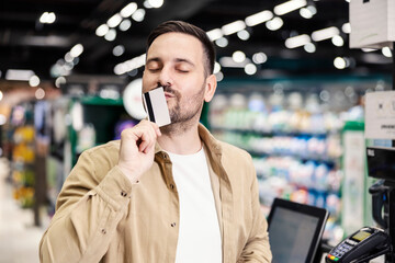 A man kissing credit card at supermarket. - obrazy, fototapety, plakaty