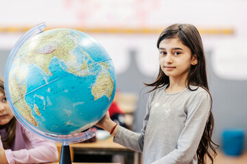 An Indian girl posing next to a globe on a geography class.