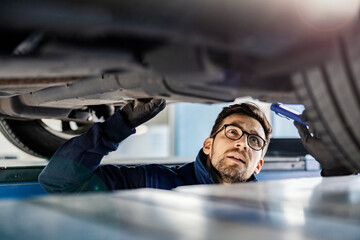 A focused auto mechanic in mechanic's pit looking at malfunction on car.
